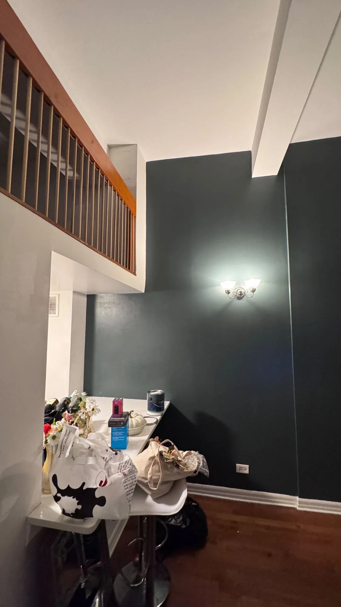 Tall deep teal accent wall in an apartment with a mezzanine railing above, white ceiling beams and trim, and dark hardwood floors