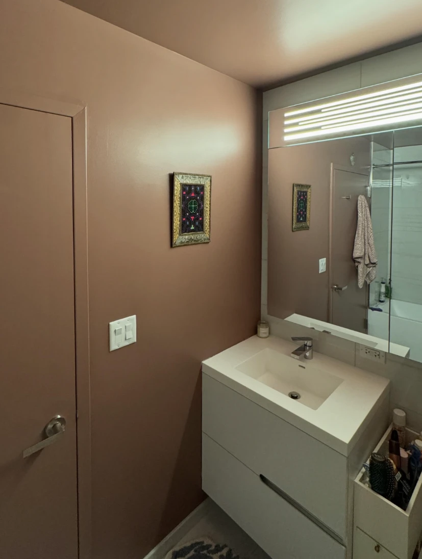 The same apartment bathroom after painting, with walls, ceiling and door in a warm dusty rose above a white vanity