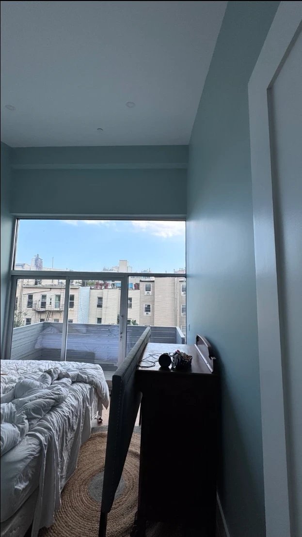 Bedroom with soft aqua walls and a header beam, a large corner window with a balcony view, and white door trim