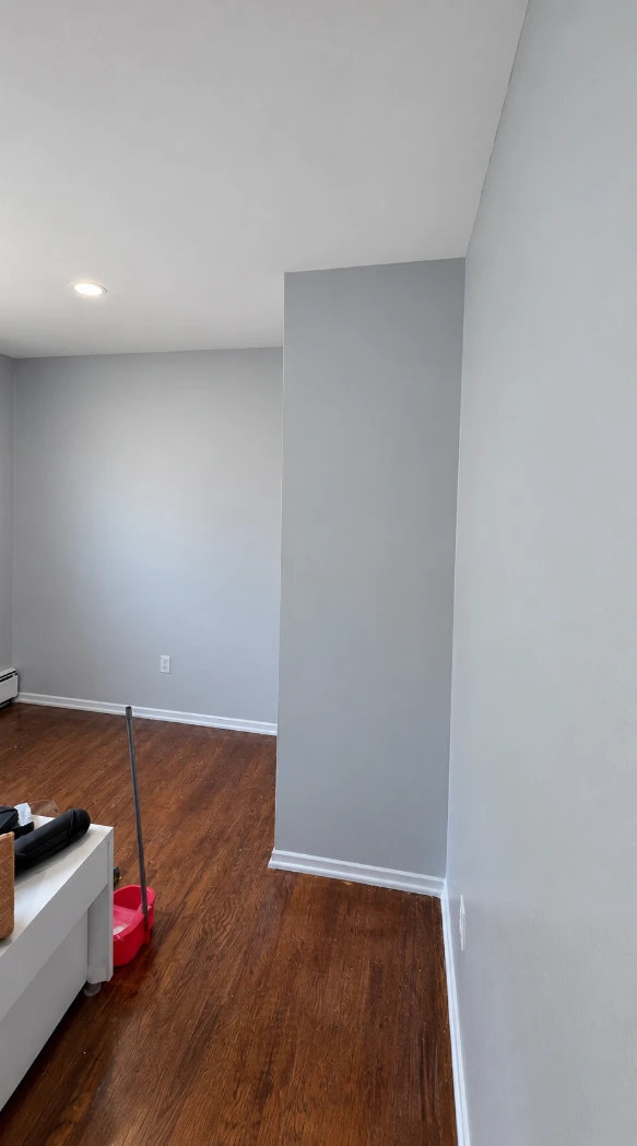 Apartment bedroom with a freshly painted light gray alcove wall, clean white baseboards, a white ceiling and hardwood floors