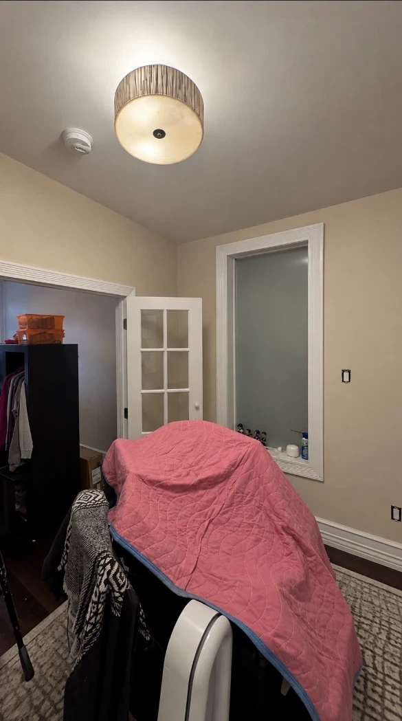 Apartment bedroom with warm taupe walls, a tall window with white trim, a white French door and furniture covered with a pink blanket