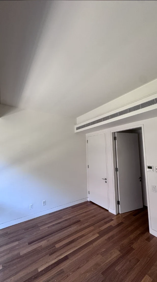 Apartment bedroom with smooth white walls and ceiling, two flat white doors with clean trim, a linear ceiling vent and warm hardwood floors