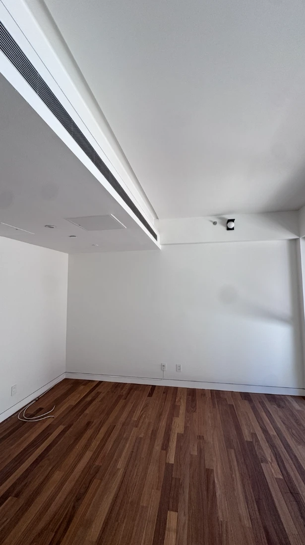 Open-plan apartment living area with smooth white walls, a stepped white ceiling with a long linear vent, white baseboards and dark hardwood floors