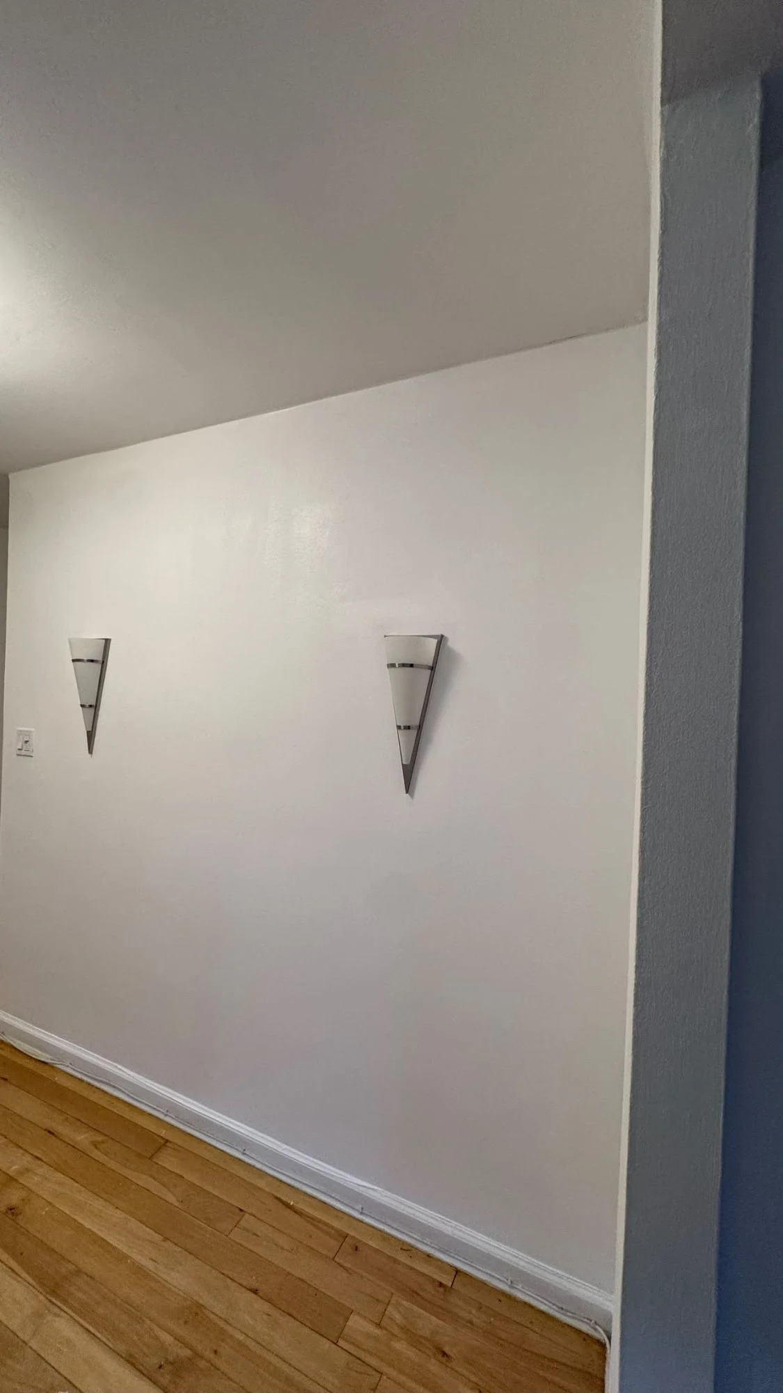Fresh white apartment wall with two modern wall sconces, a white baseboard and hardwood floors