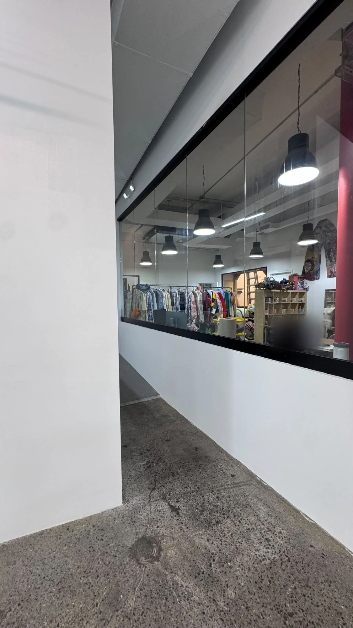 Clean white partition walls around a black-framed glass window in a commercial space, with a polished concrete floor